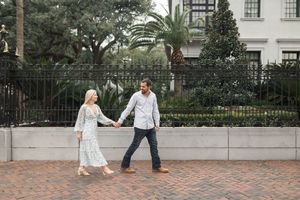 A couple strolls along a palm-lined path near a white colonial-style building.