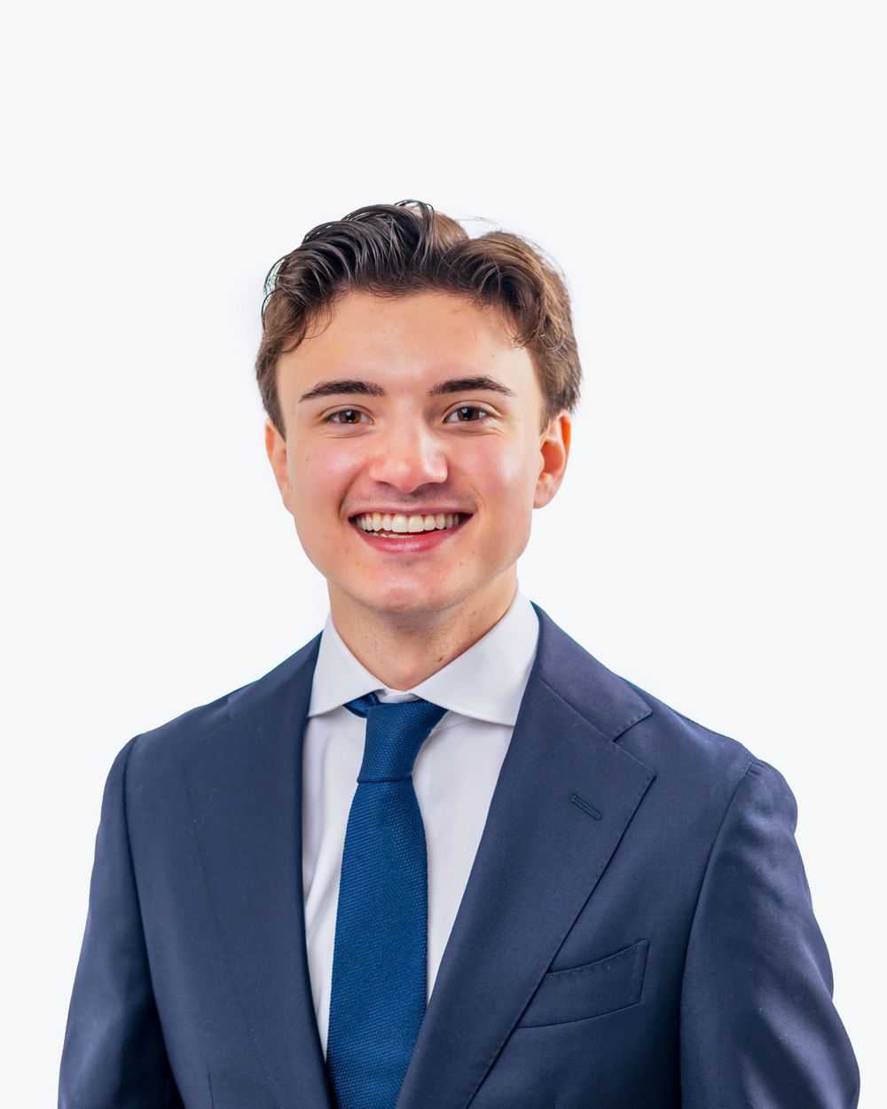 Professional headshot of someone in a navy suit with a blue tie smiling against a light background.