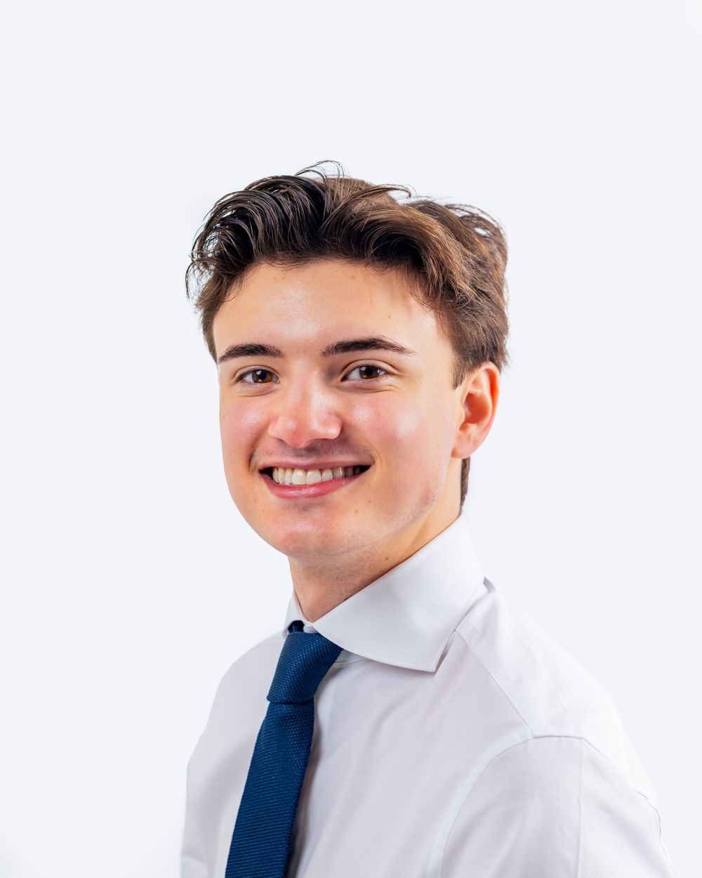 Professional headshot of a young person in business attire with white shirt and navy blue tie against light background.