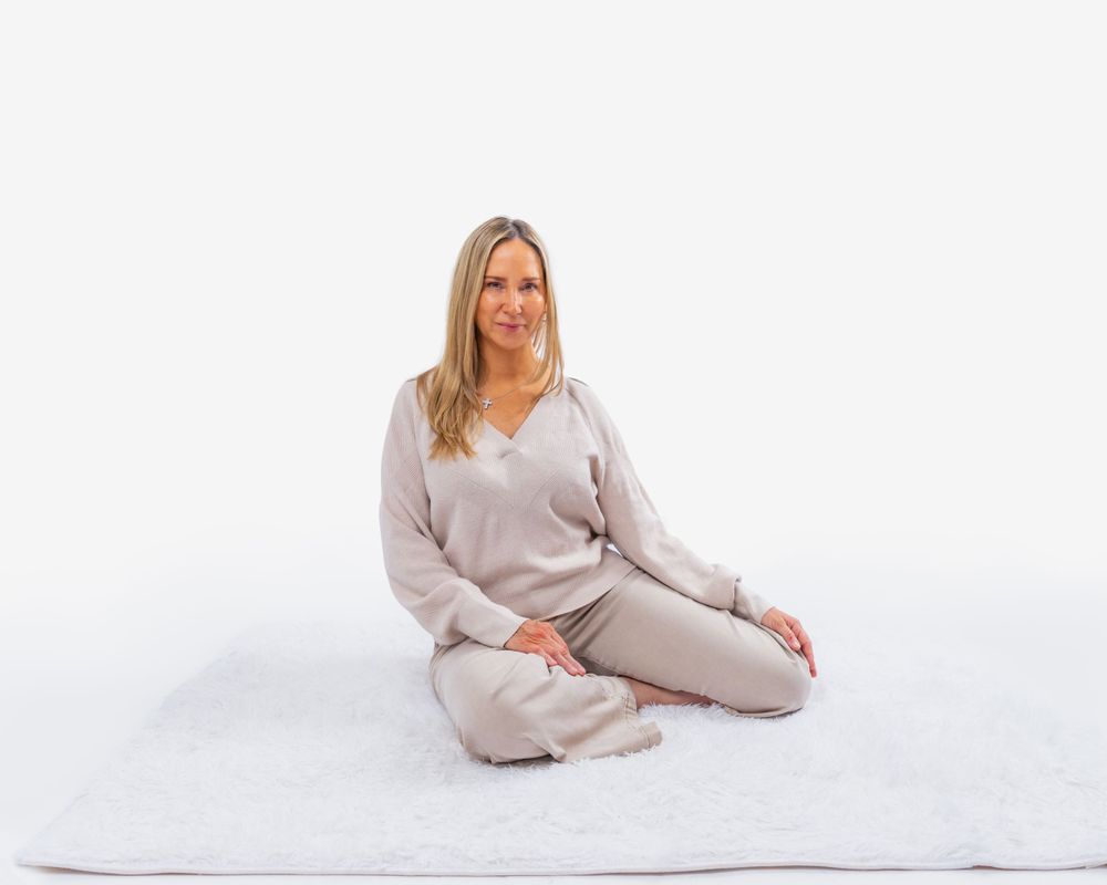 Person wearing a cozy beige knit loungewear set sits cross-legged on a white blanket against white background.