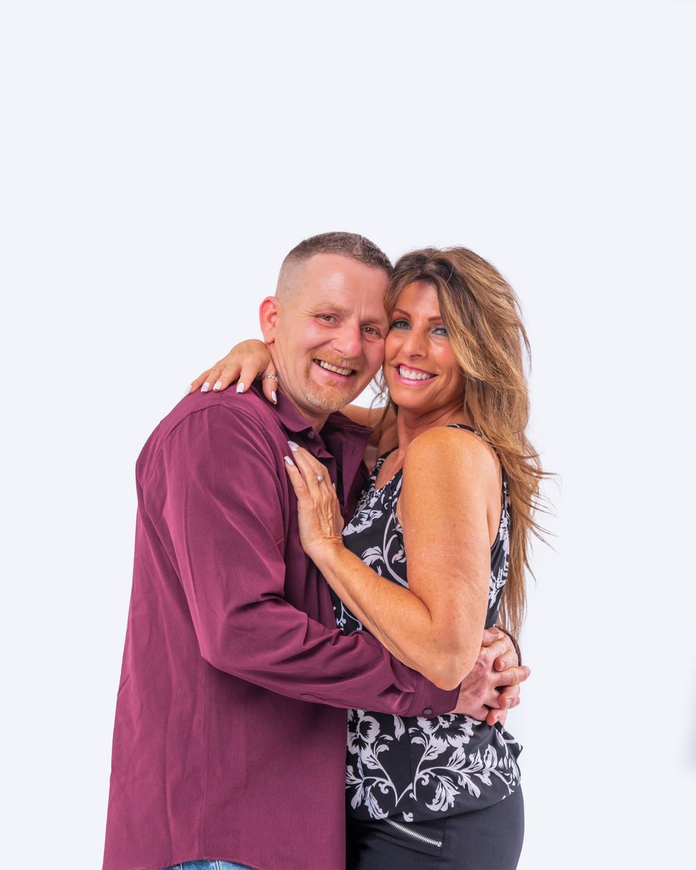 A happy couple embraces and smiles while posing against a white background for a portrait.