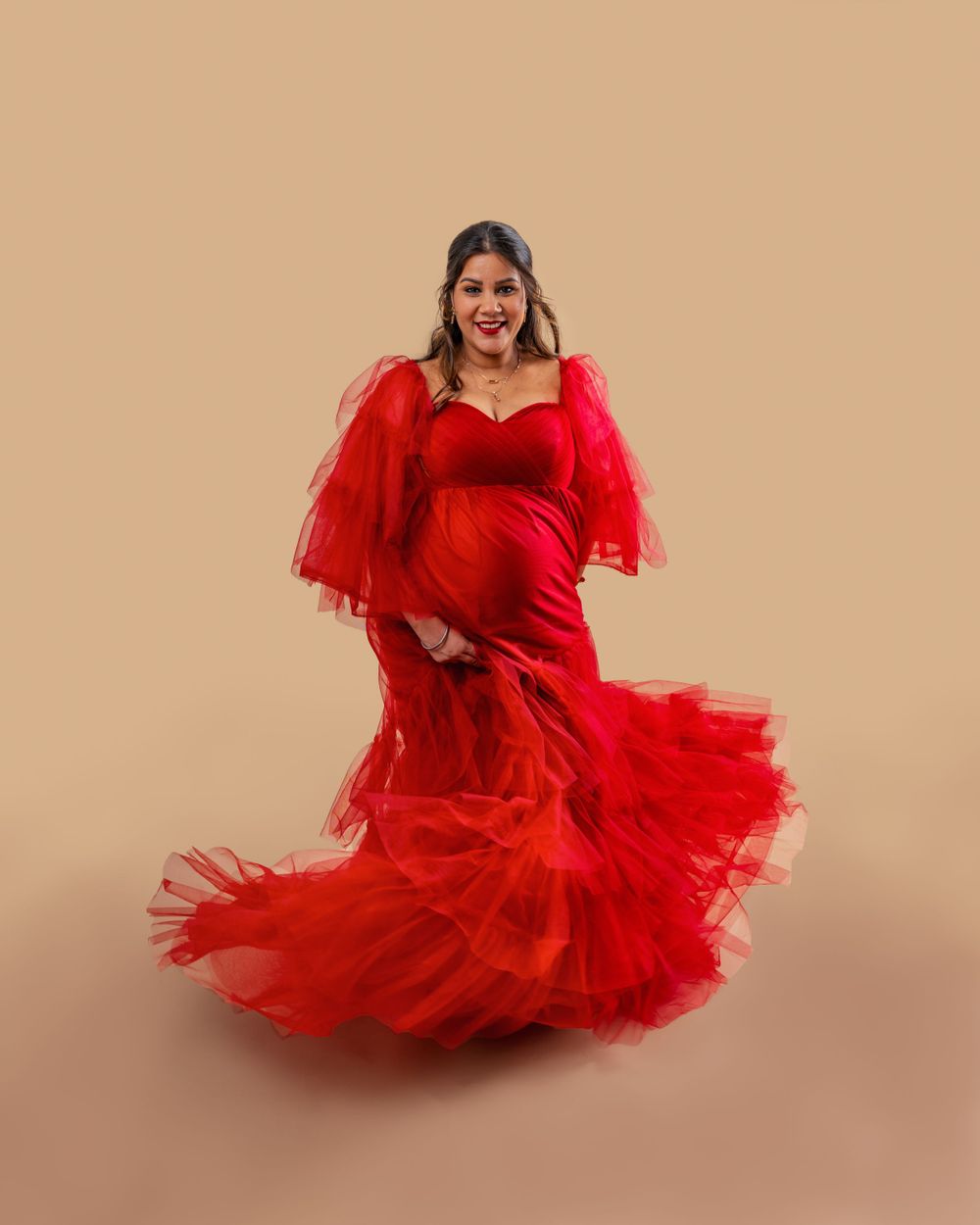 Someone in a dramatic red tulle gown with flowing ruffles poses gracefully against a neutral background.