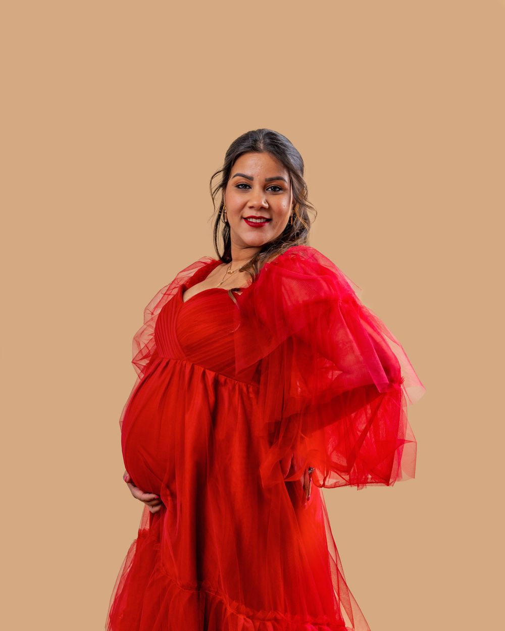 Woman in a flowing red tulle dress poses against a neutral beige background.