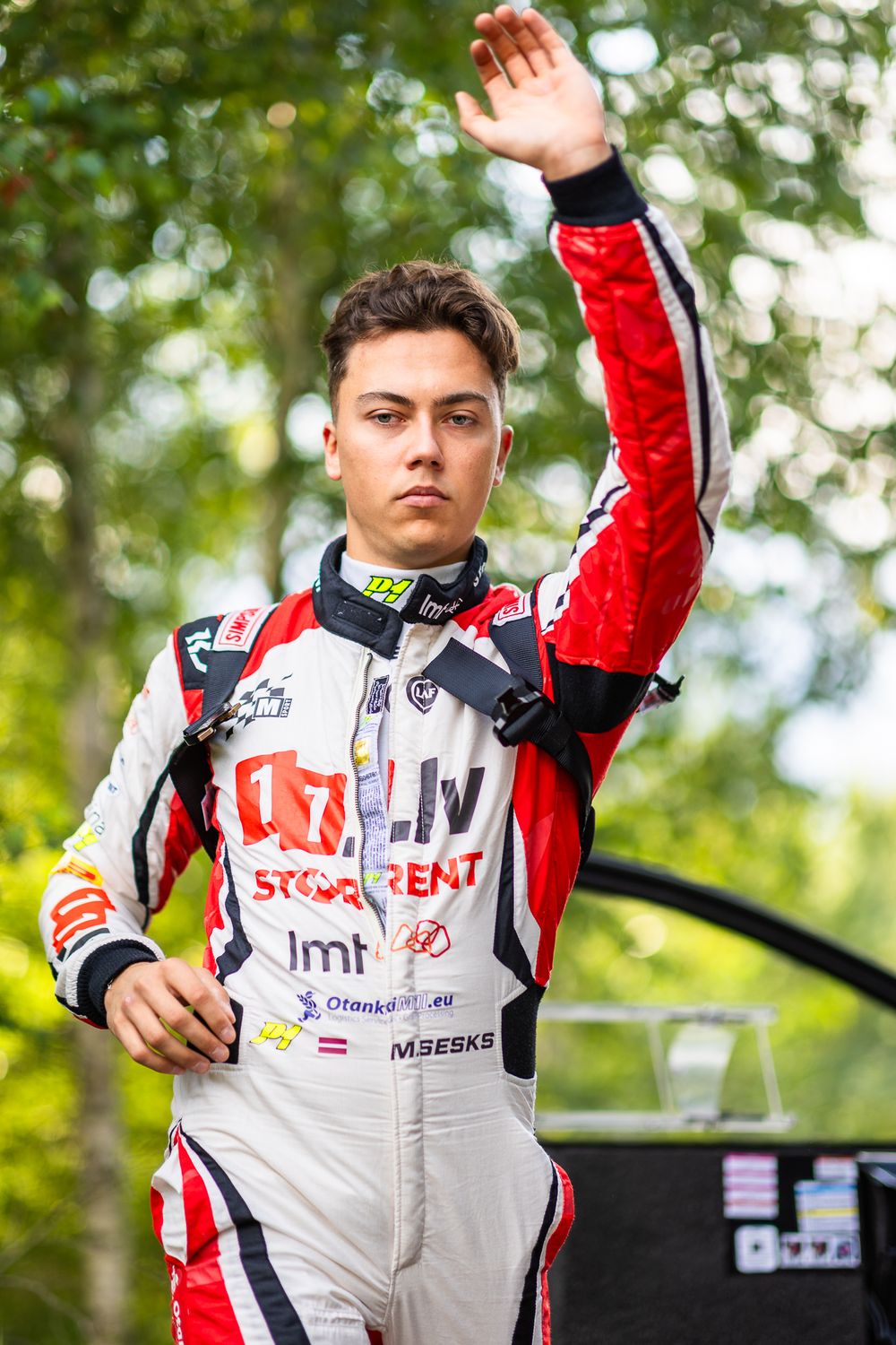 Rally driver in white and red racing suit waving to crowd.