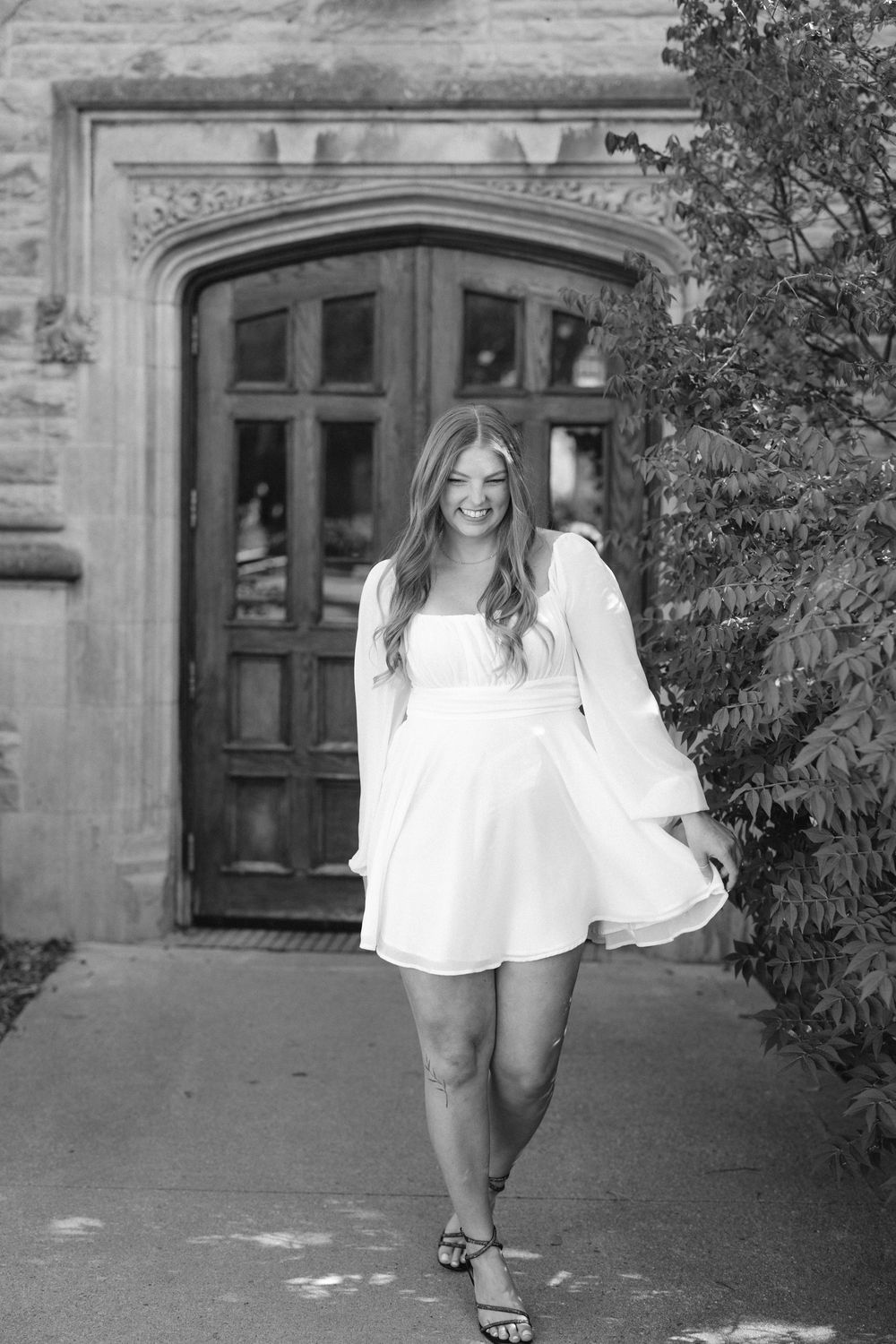Black and white photo of someone in a white summer dress standing in front of an ornate wooden doorway.