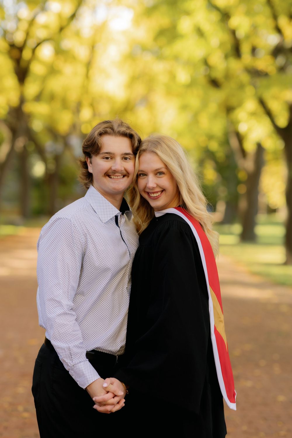 A couple shares a joyful moment together on an autumn day with golden trees in the background.