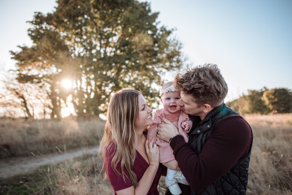 Family embraces and laughs together in sunlit field during golden hour.