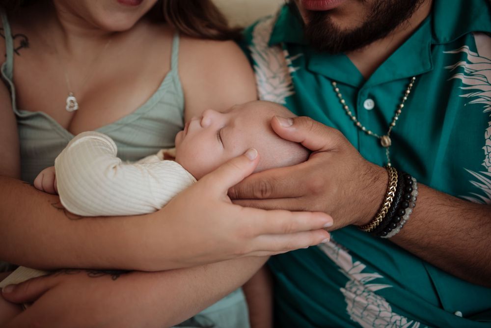 Close-up of hands tenderly holding small infant in tropical print setting.