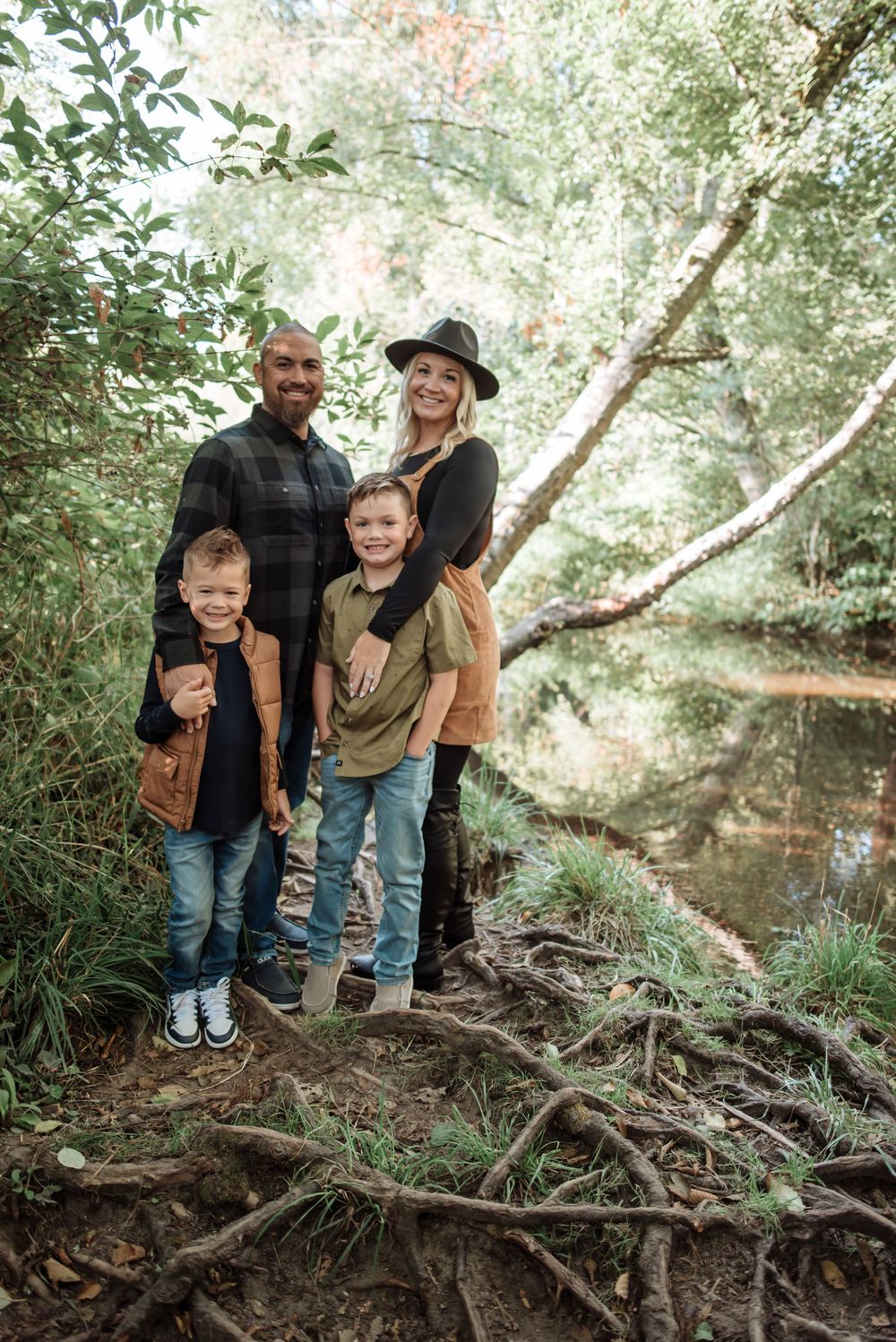 A family poses for an outdoor portrait by a creek surrounded by lush greenery.