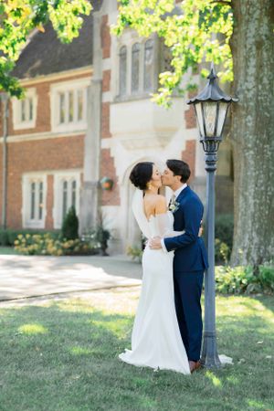 Romantic wedding portrait by vintage lamppost near brick building with lush greenery.