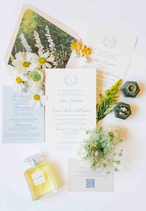 Wedding invitation suite with daisies, perfume bottle and delicate floral arrangements on white background.