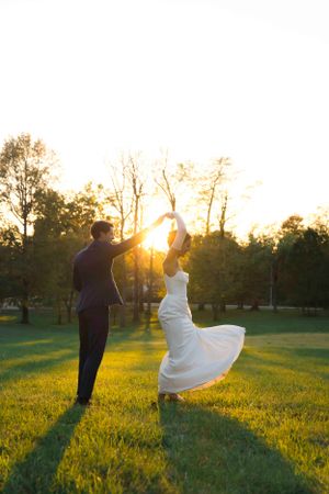 Silhouette of dancing couple in wedding attire against golden sunset in a grassy field.