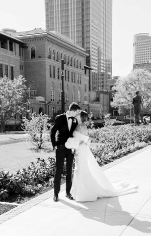 Black and white wedding photo with urban architecture and blooming trees in background.