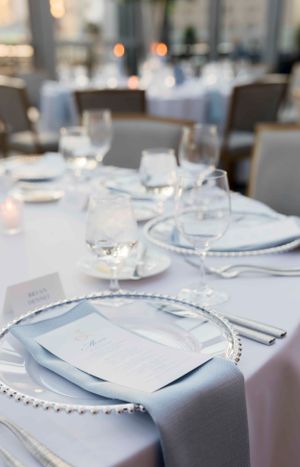 Elegant place setting with beaded charger plate and menu card in soft blue and white tones.
