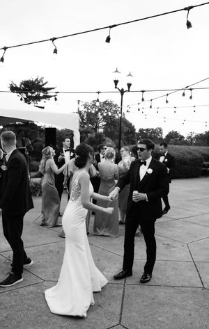 Wedding guests dancing outdoors under string lights and lamp posts at an evening reception on a patio.