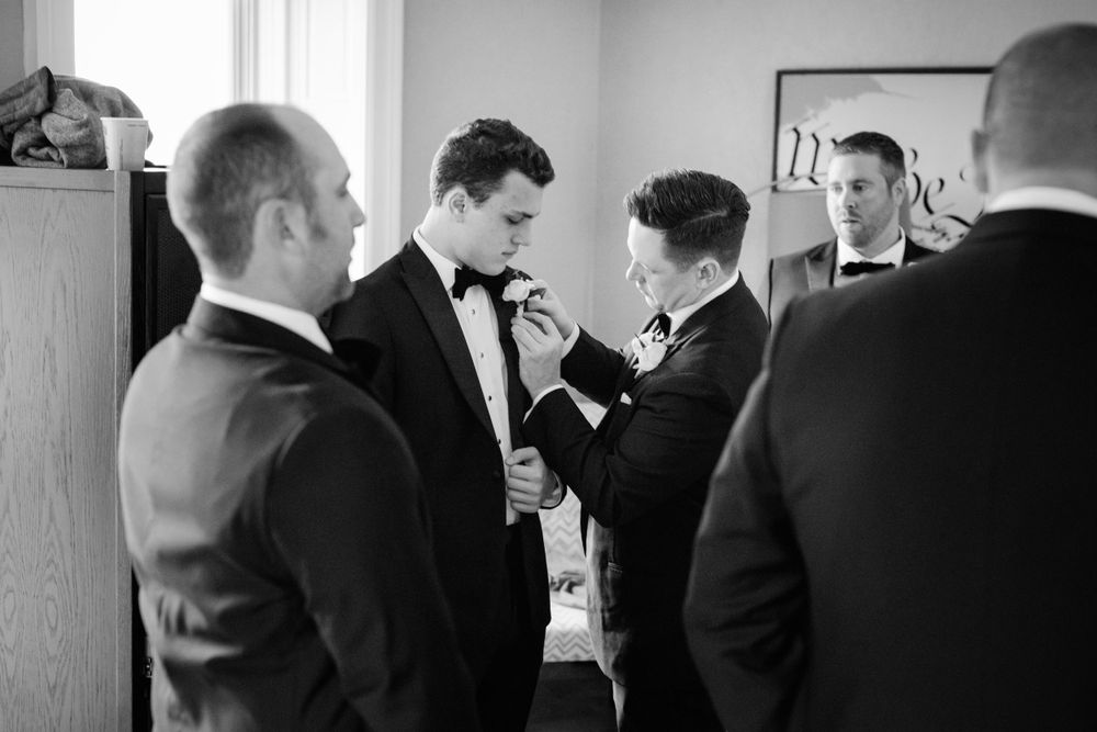 Black and white photo of groomsmen adjusting their bowties and getting ready before a formal wedding ceremony.