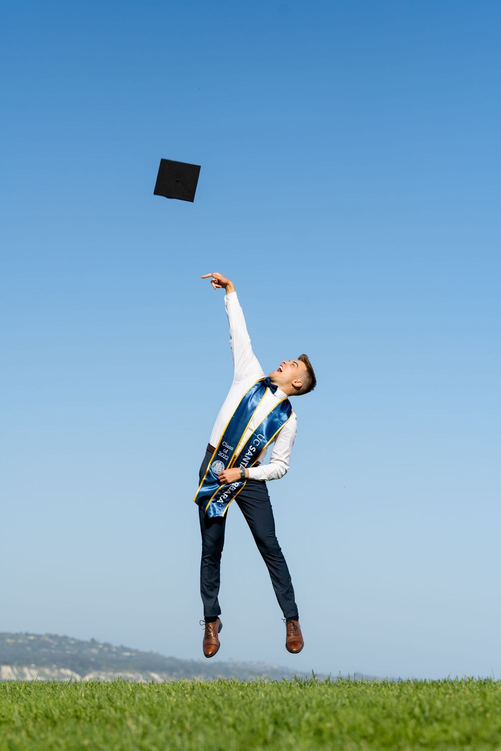 A person in business attire bends backwards dramatically while tossing a black object into the bright blue sky.