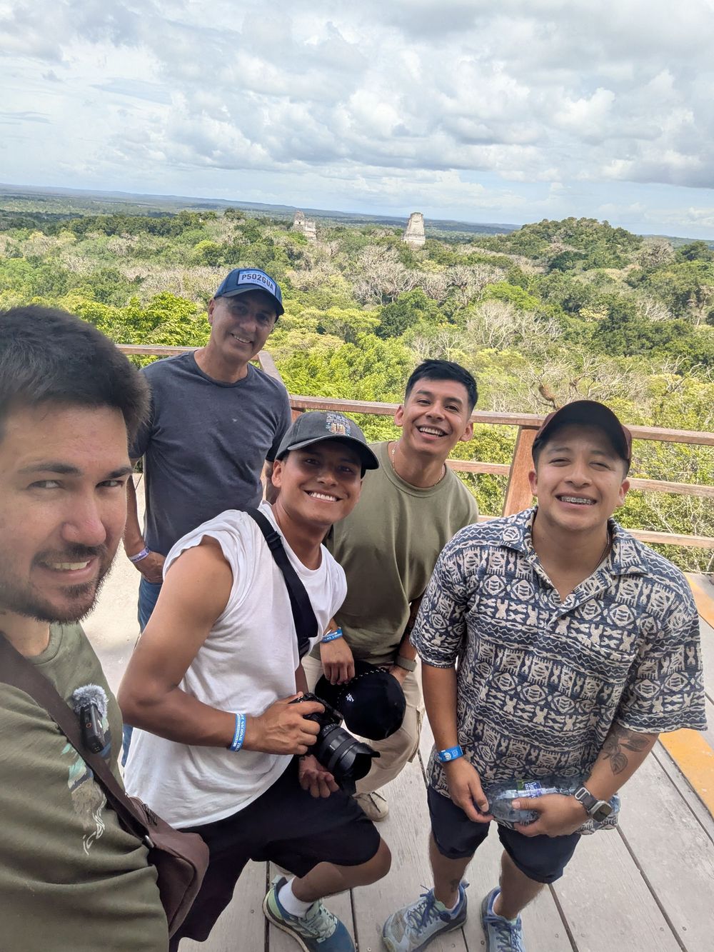 A group of people enjoying a scenic overlook on a sunny day with lush green landscape and buildings in the distance.