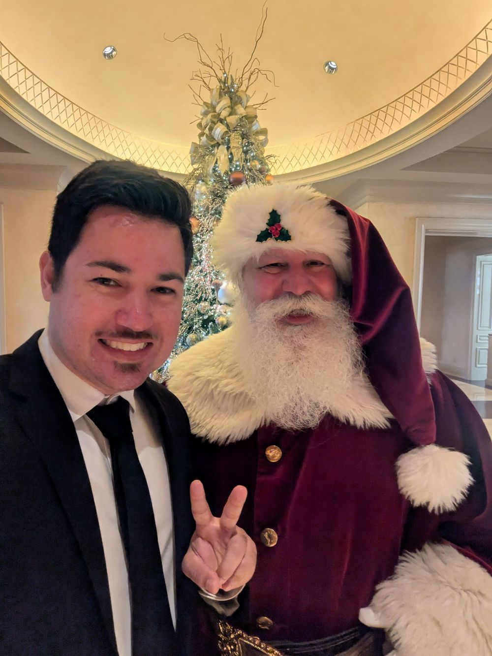 A festive holiday scene with a traditional Santa Claus figure in burgundy robes next to a decorated Christmas tree.