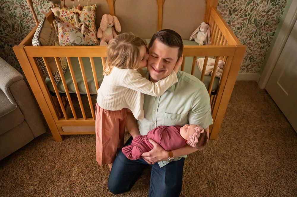 A parent and child share a tender moment while sitting in front of a wooden crib in a cozy nursery.