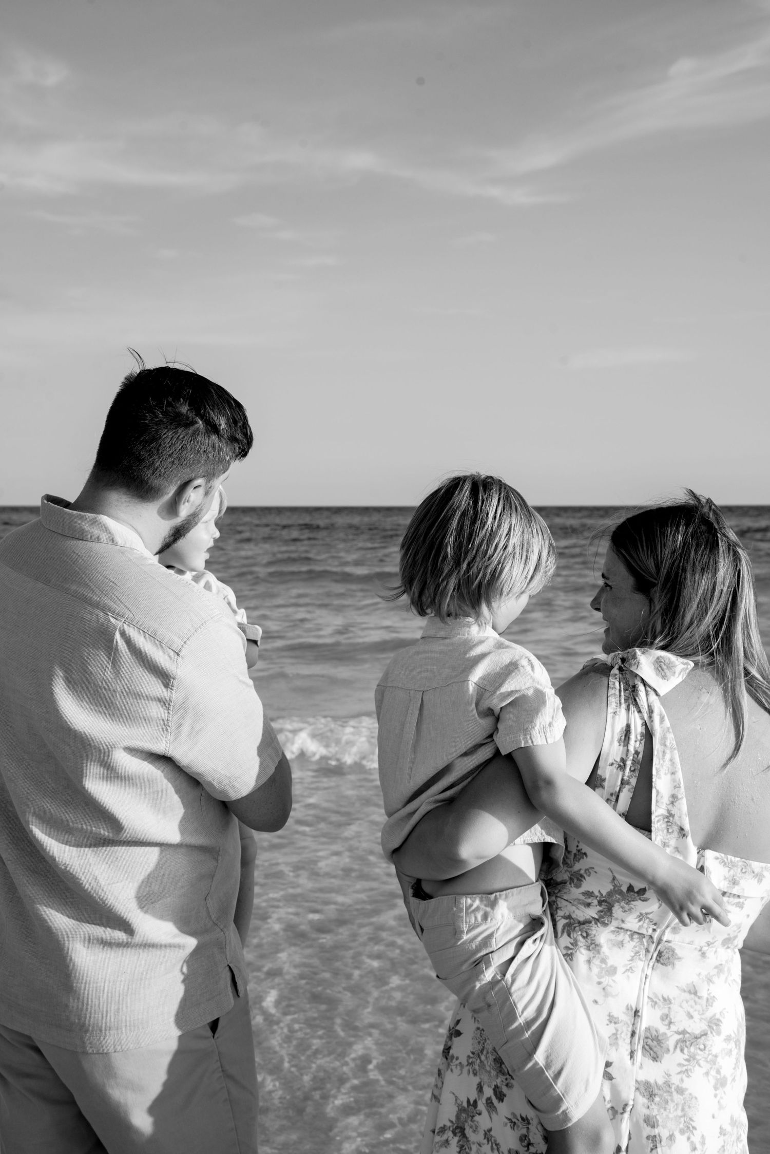 Black and white beach scene with people looking out at ocean waves.