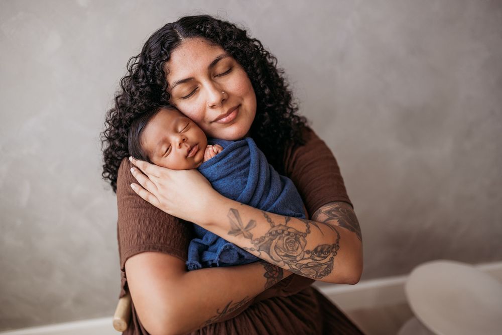 mother holding newborn close to her face while newborn is wrapped in a blue swaddle.