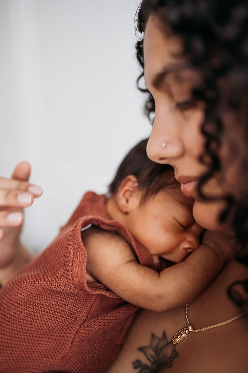 newborn cuddling into mother's chest wearing a rust outift