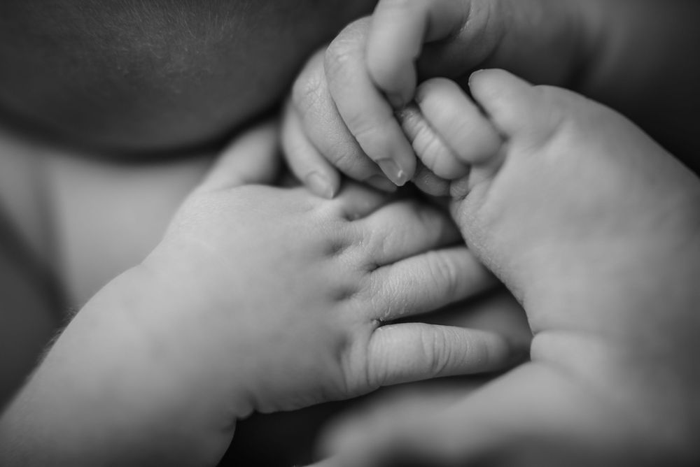 newborn hands holding onto her toes close up.