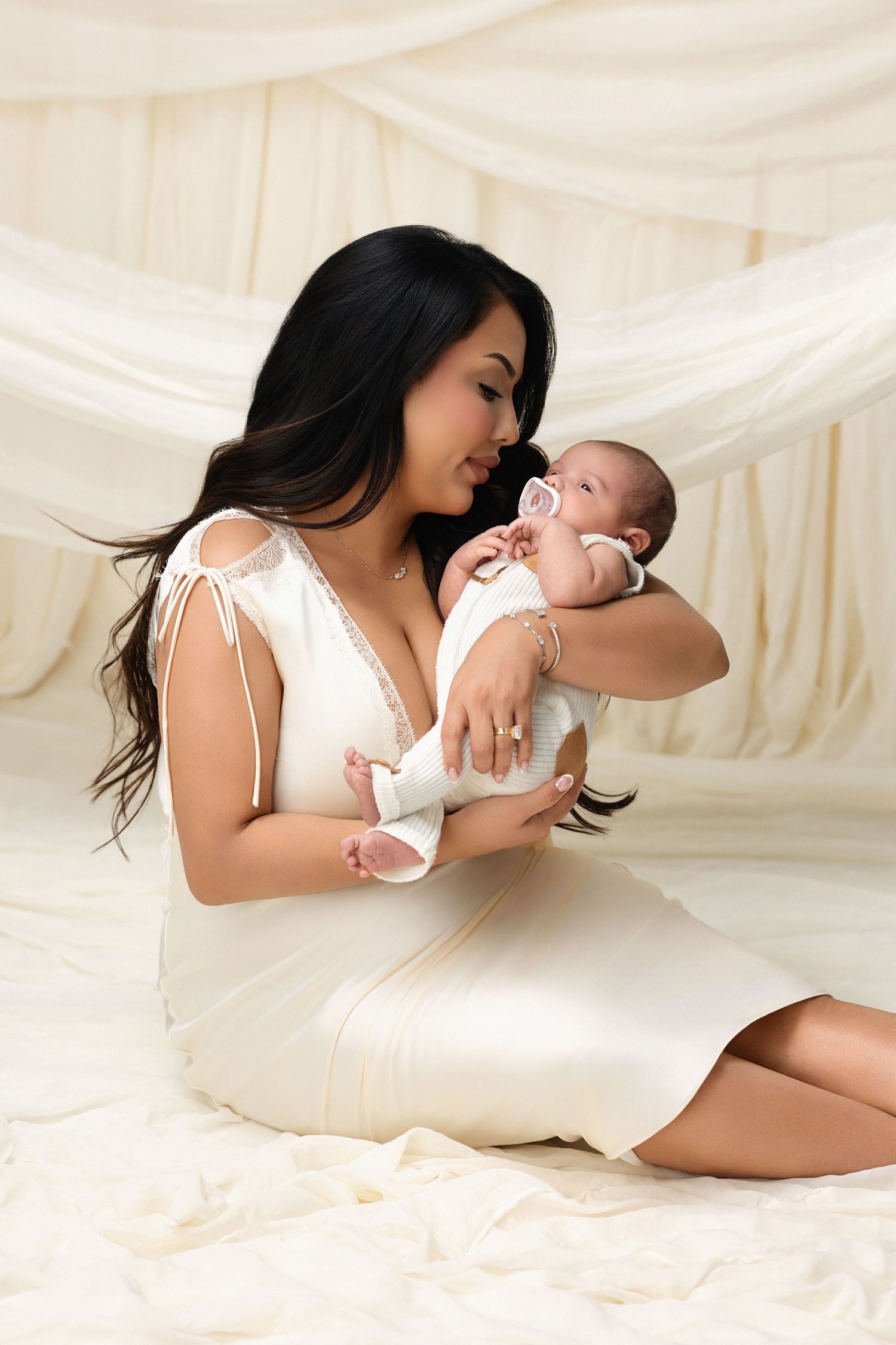 A tender moment captured between parent and baby in black outfits against a white backdrop with dramatic shadow.