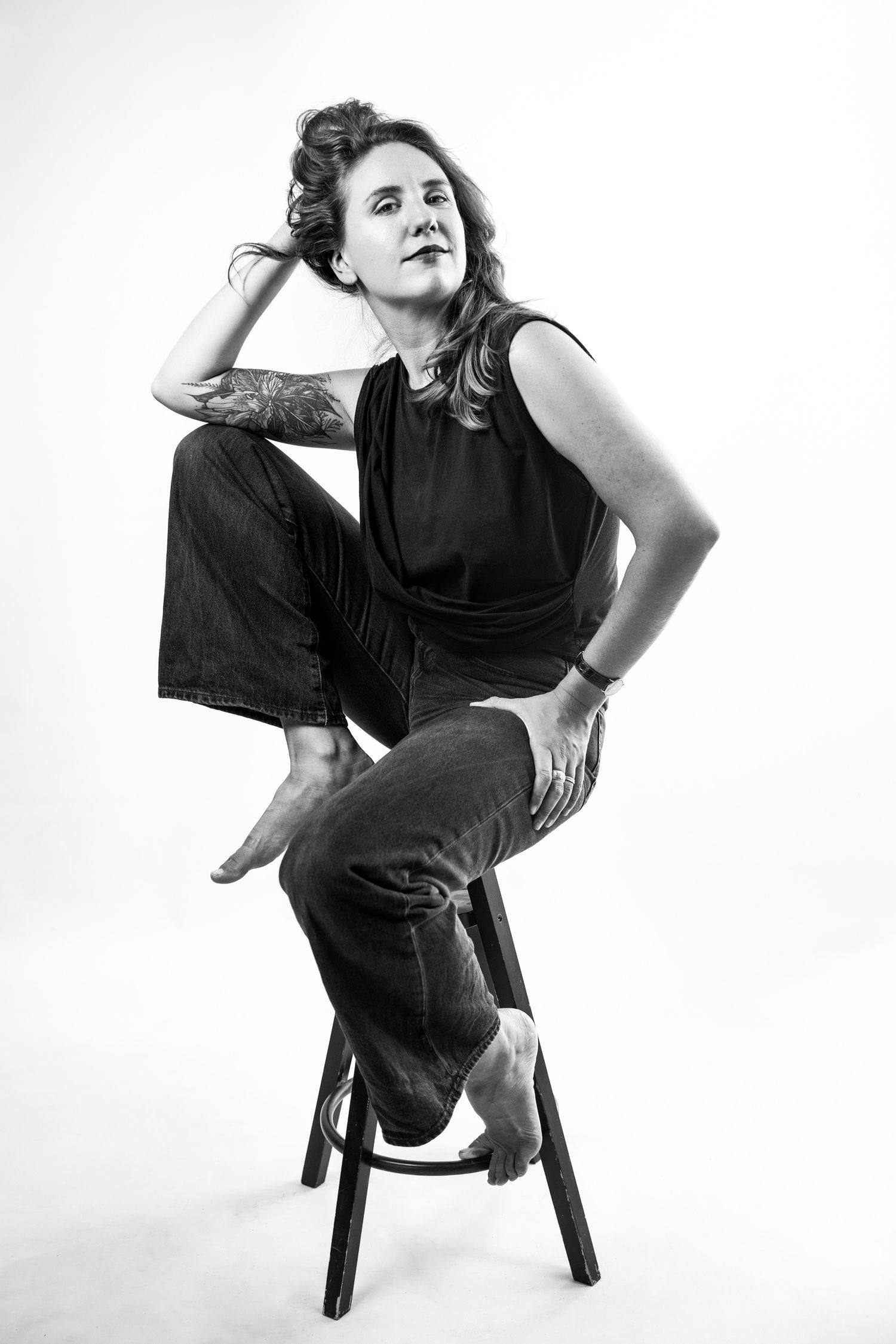 Black and white studio portrait of a woman seated on a high stool; professional personal branding and minimalist headshot.