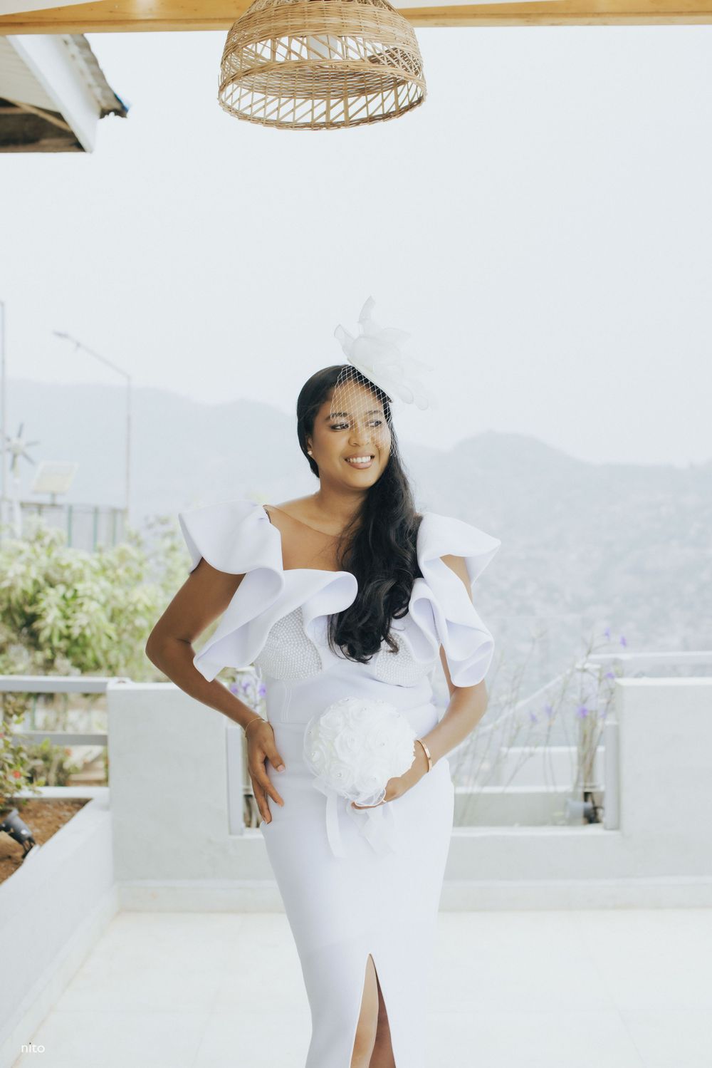 A bride in a modern white dress with ruffled details poses on a bright terrace.