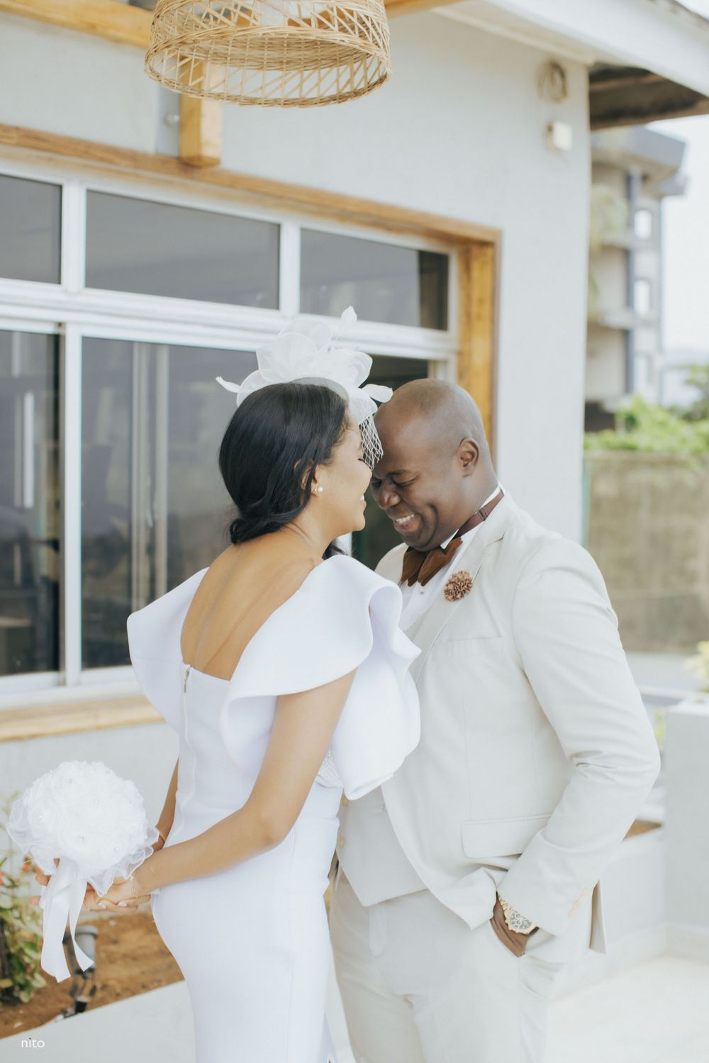 A romantic wedding couple in all white outfits share an intimate moment on a bright outdoor terrace.