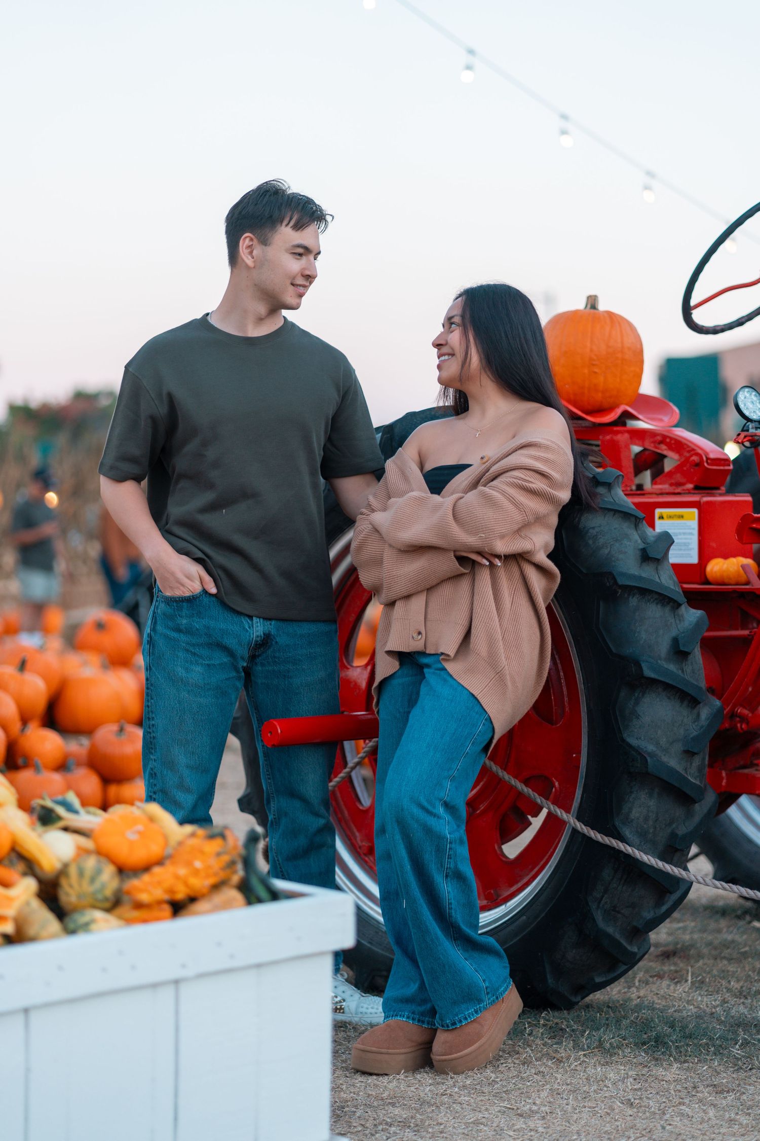 Casual couple photoshoot at a pumpkin patch with vintage red tractor in background.
