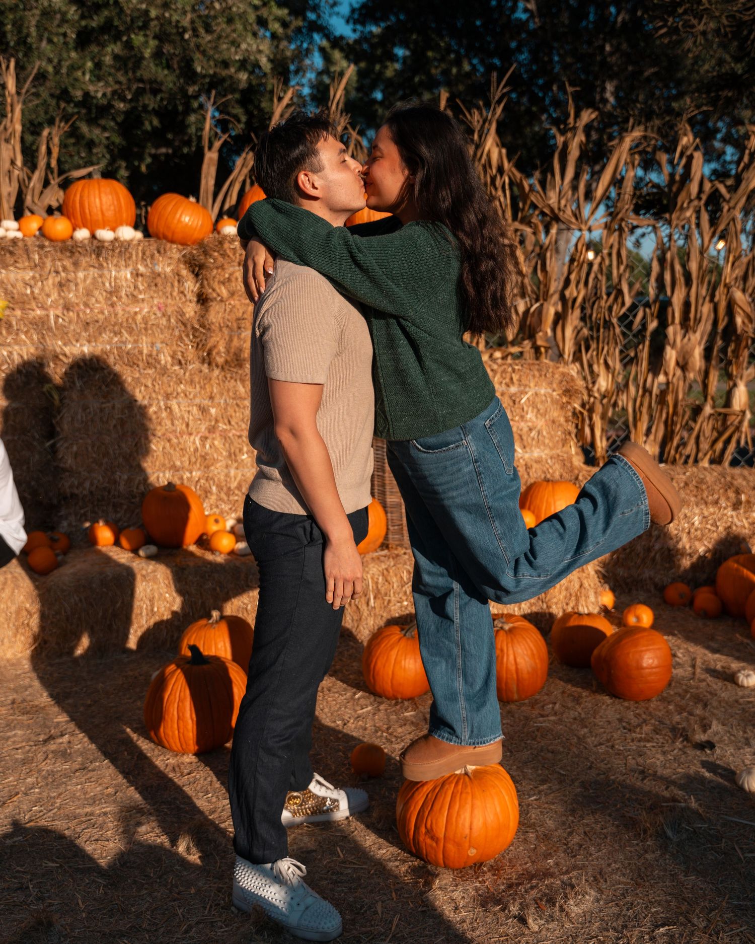 Couple sitting among autumn pumpkins at sunset in a rustic outdoor setting.