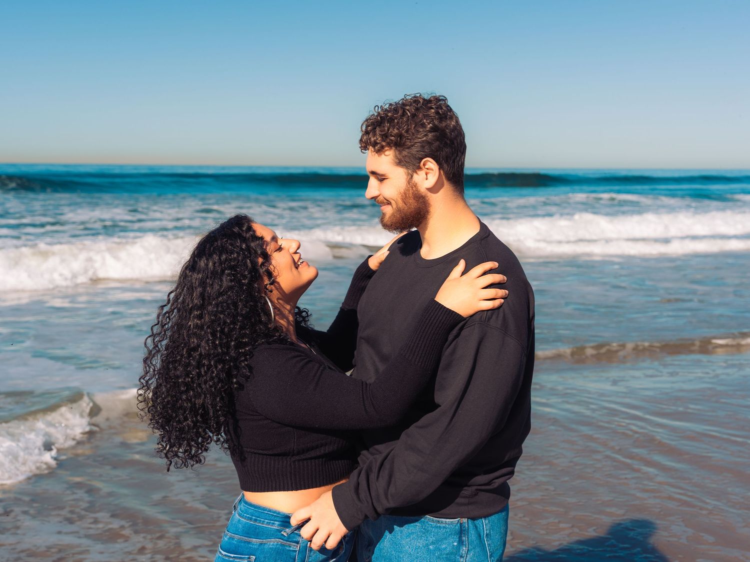 Couple shares tender moment on sandy beach with ocean waves rolling in.