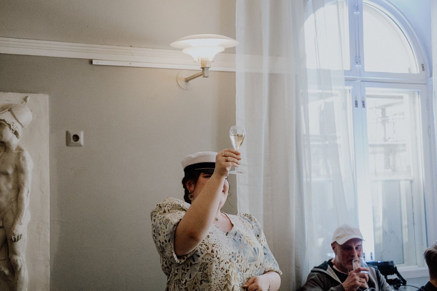 People raising wine glasses in a bright sunlit room with arched windows during a celebration.