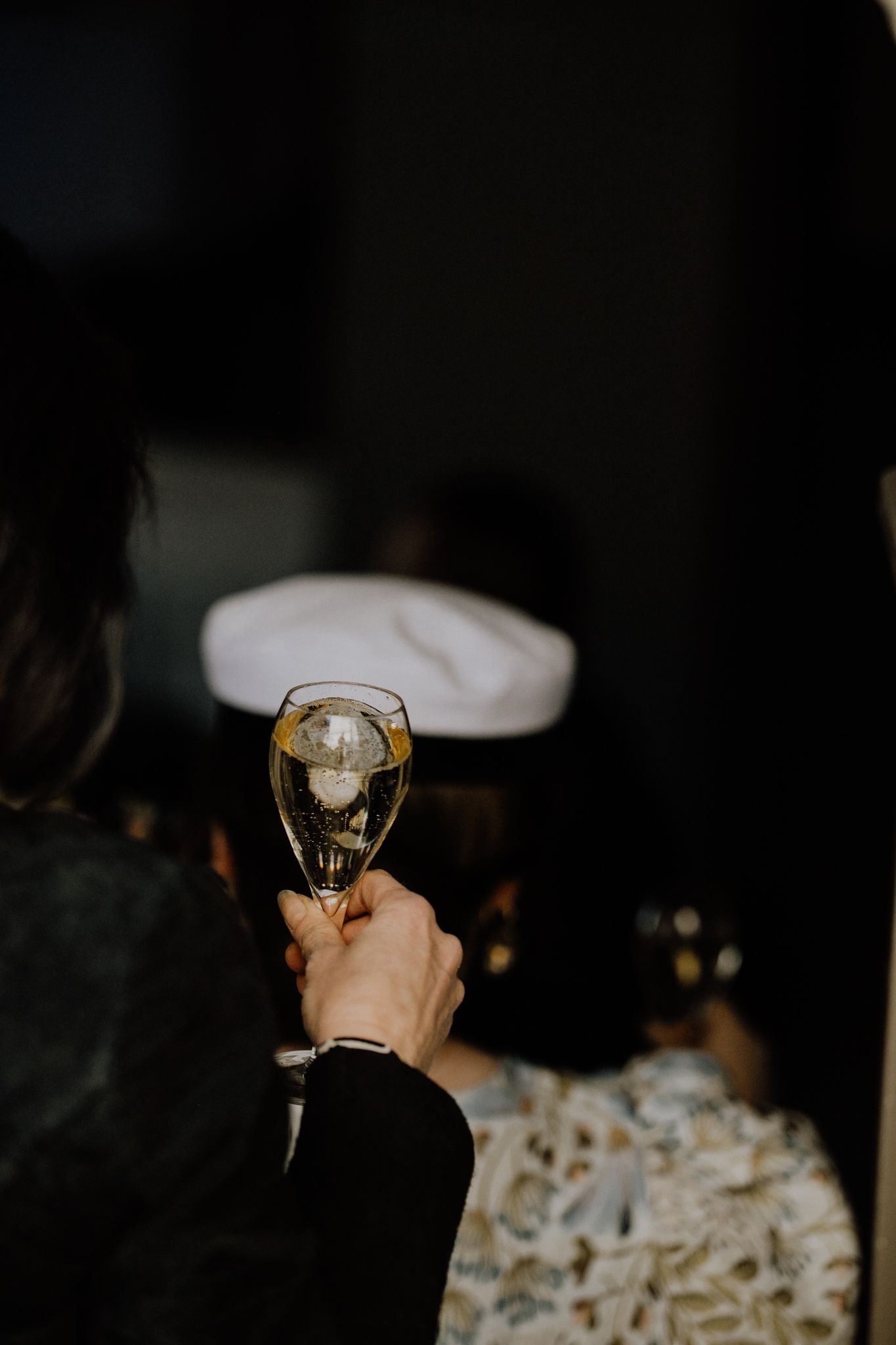 Hand holding a wine glass against a dark background in a moody setting.
