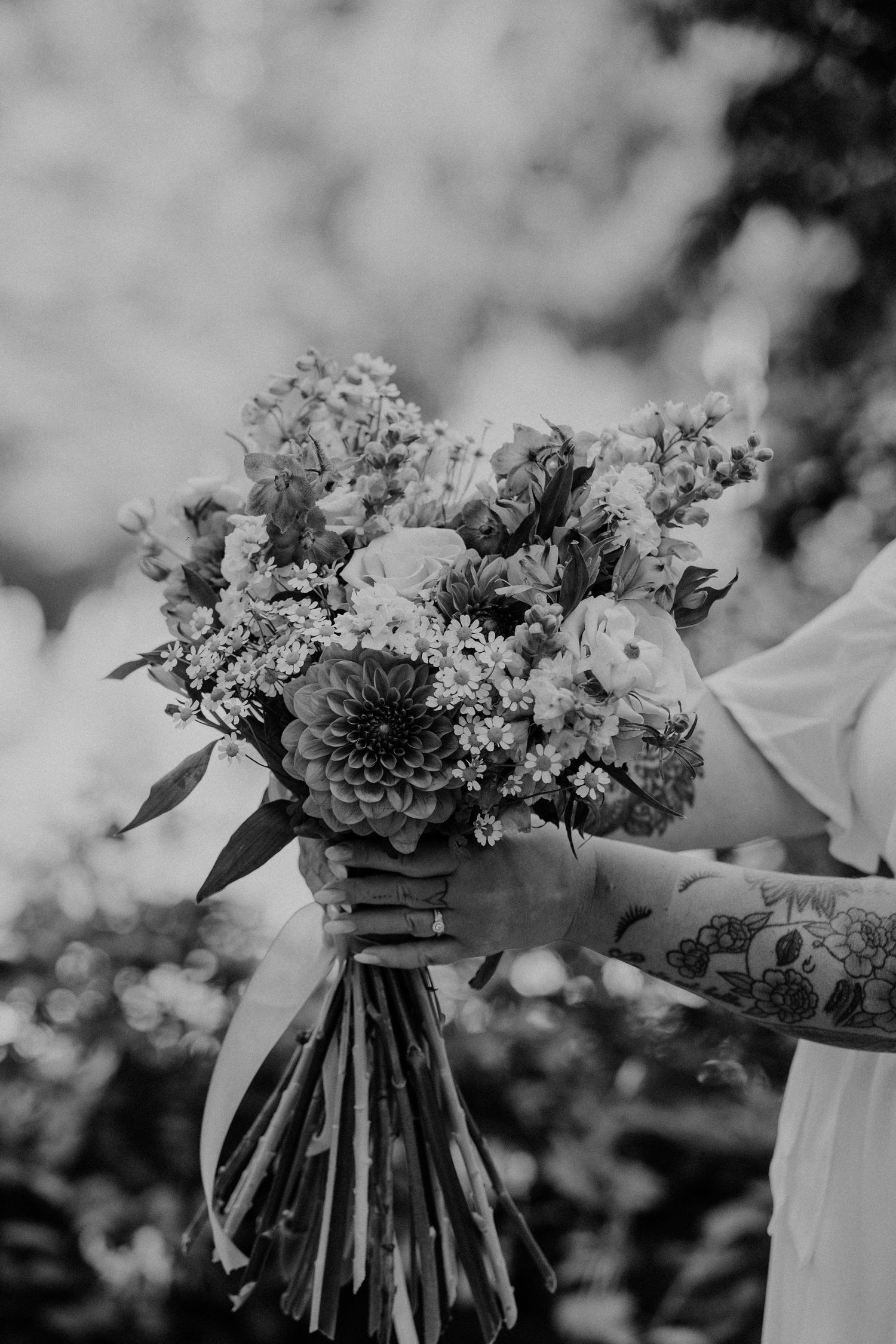 A row of bridesmaids holding white floral bouquets in an outdoor garden setting, shown in black and white.