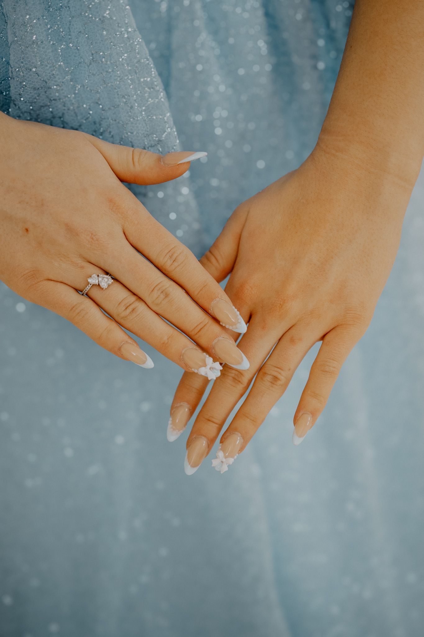 Close-up view of elegant bridal hands displaying diamond rings against soft blue fabric background.