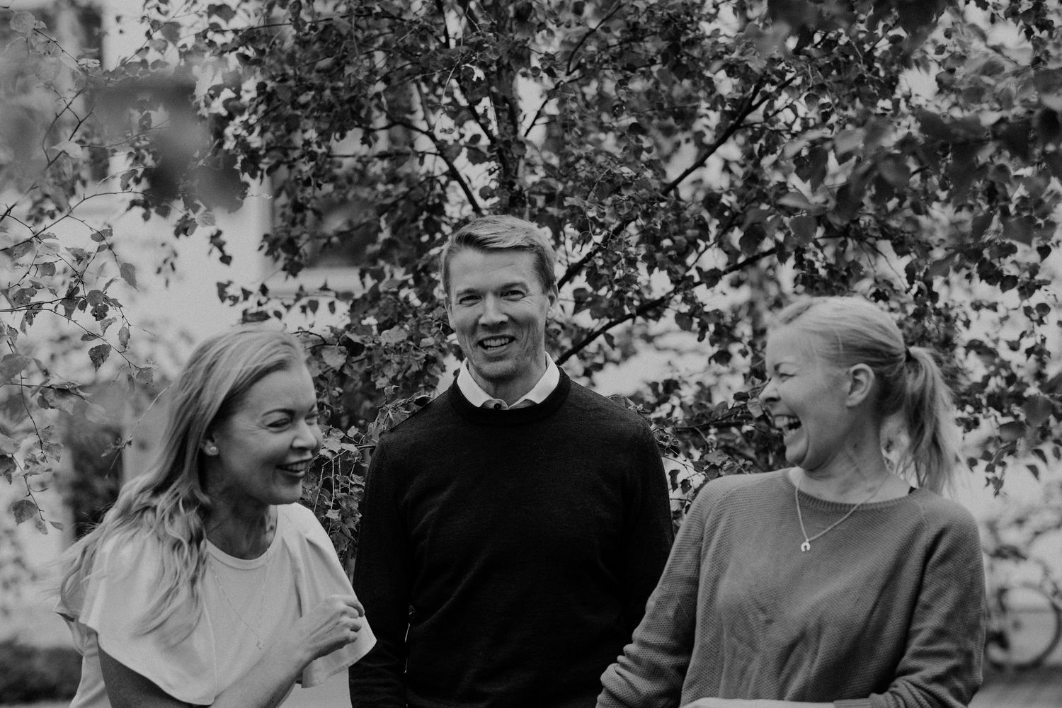 Black and white photo sequence showing joyful expressions and laughter in an outdoor setting with trees in background.