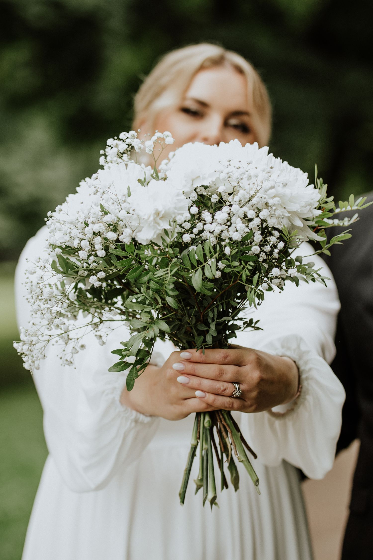 A beautiful white bridal bouquet with baby's breath flowers held against a white dress outdoors in a garden setting.