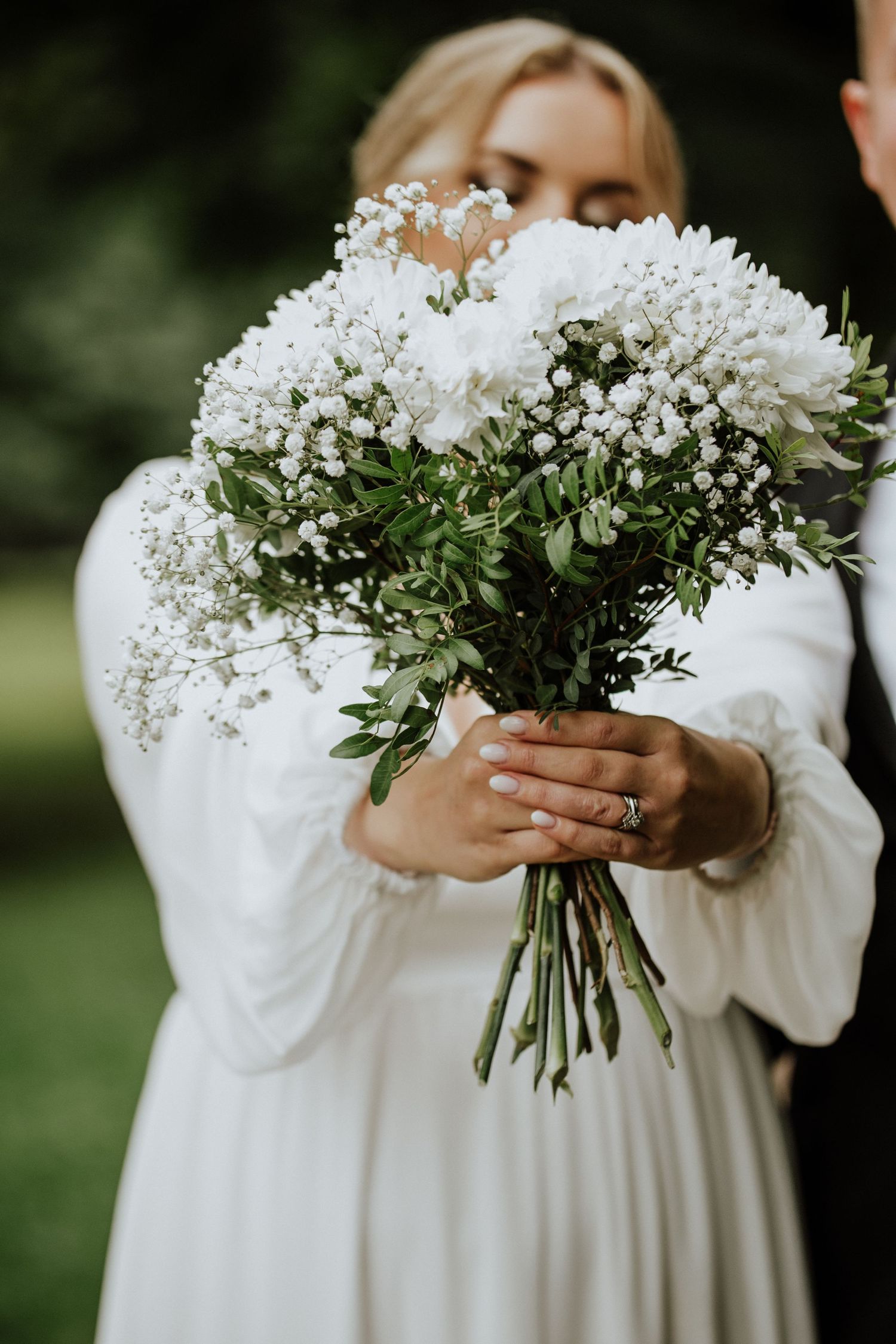 Elegant white and green bridal bouquet held against wedding dress.