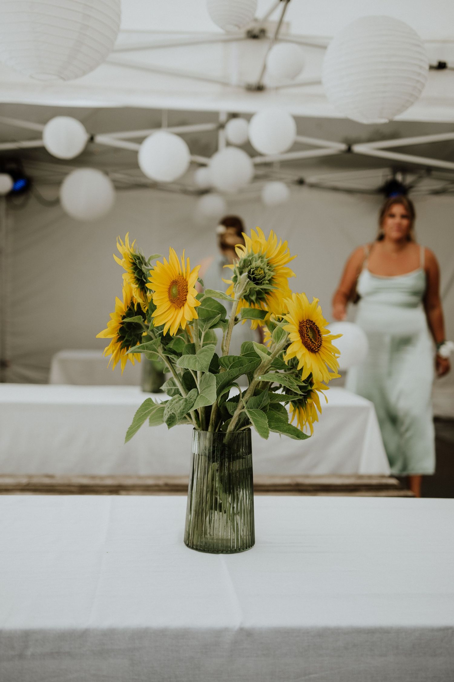 Sunflower arrangement in glass vase with white paper lanterns overhead.