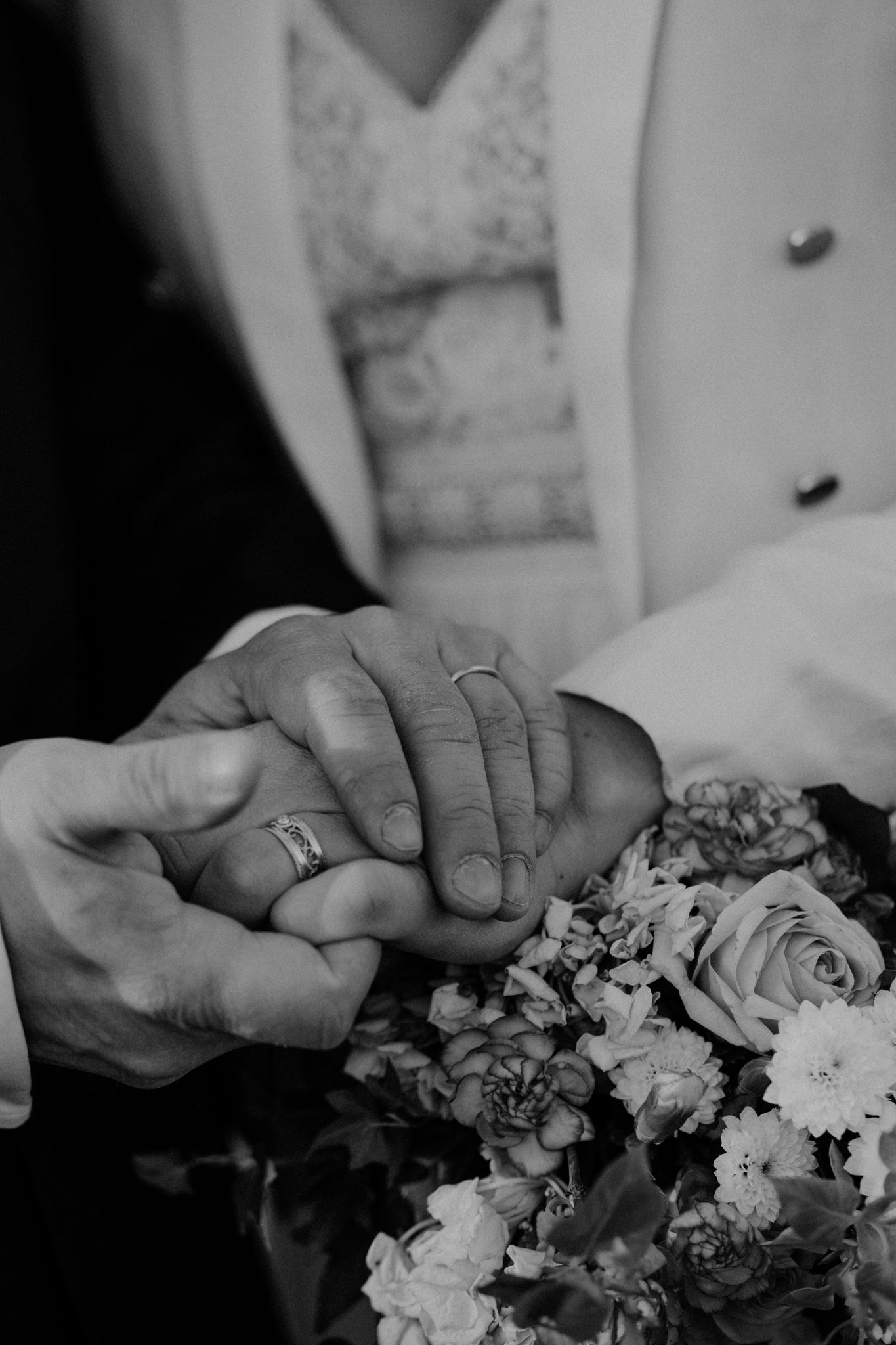 Black and white close-up photos of hands holding a floral bouquet with roses and white flowers.