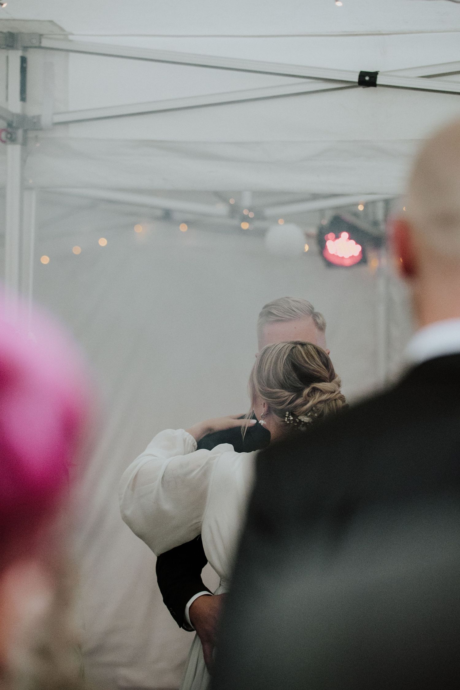 A tender moment captured during a wedding reception under a white tent with twinkling lights.