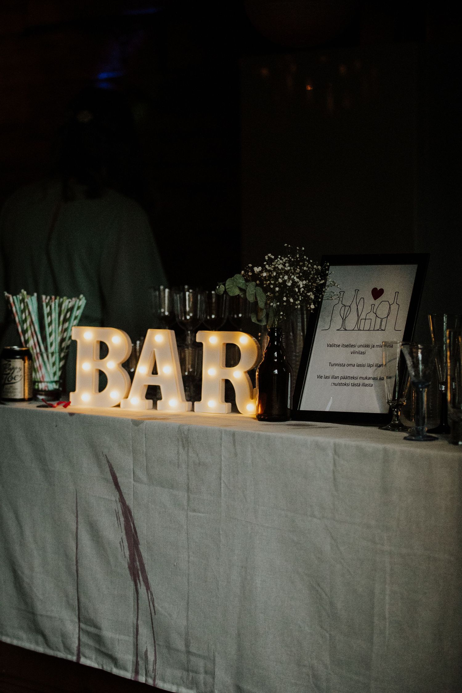 Illuminated BAR sign with striped straws and glassware at a wedding reception.