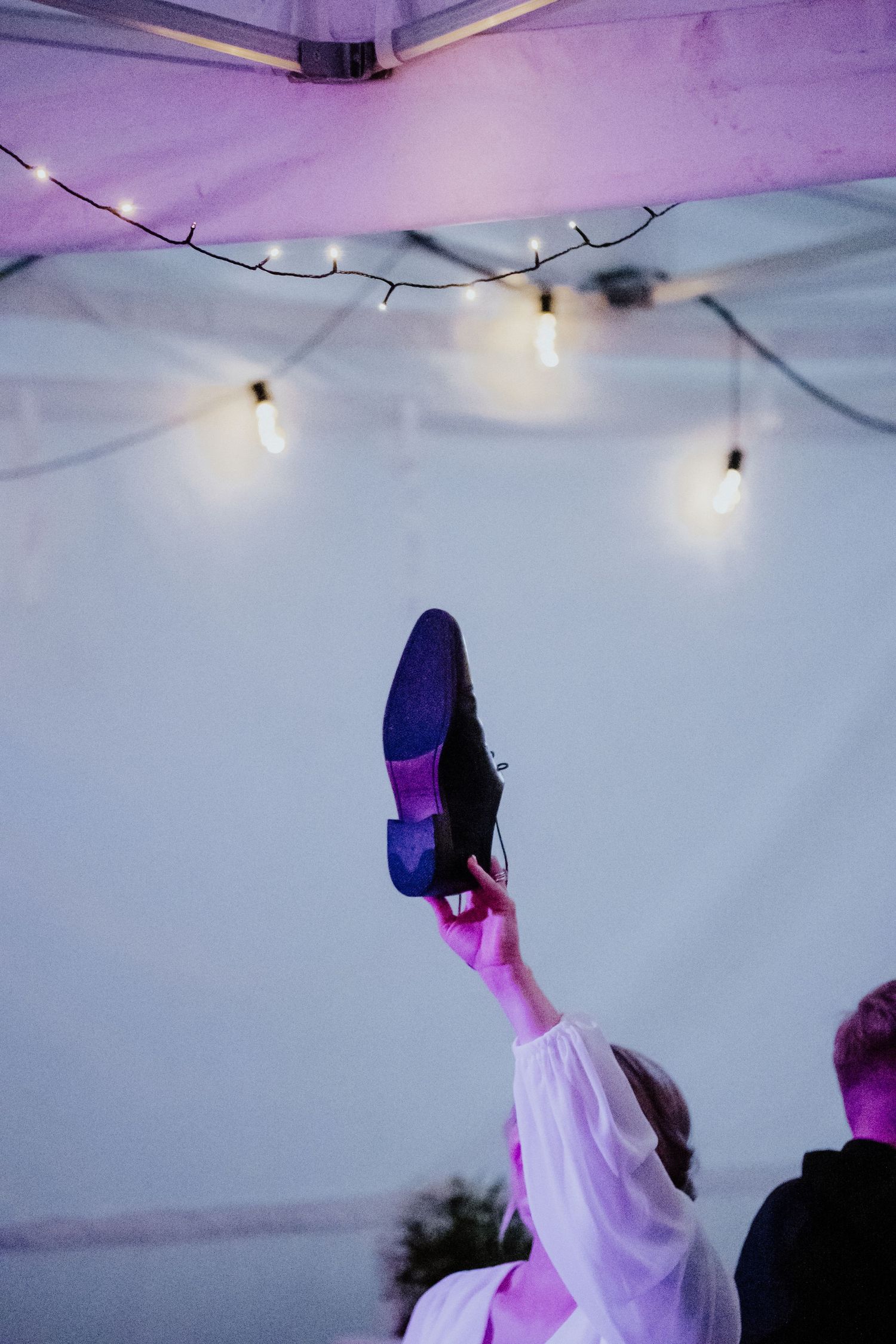 A shoe held up high under string lights during a wedding celebration.