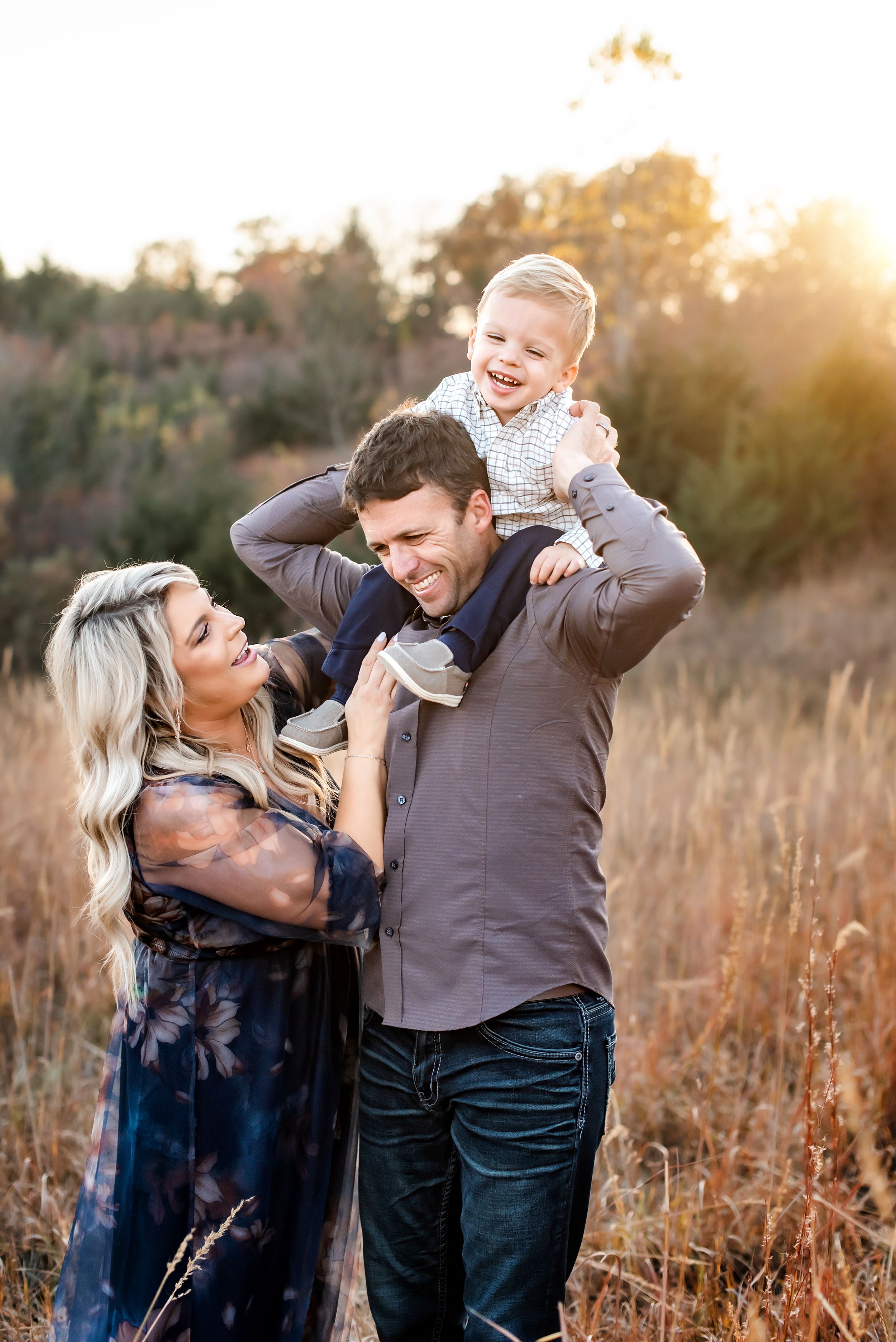 Family shares joyful moment in golden sunset light among tall grass in outdoor nature setting.