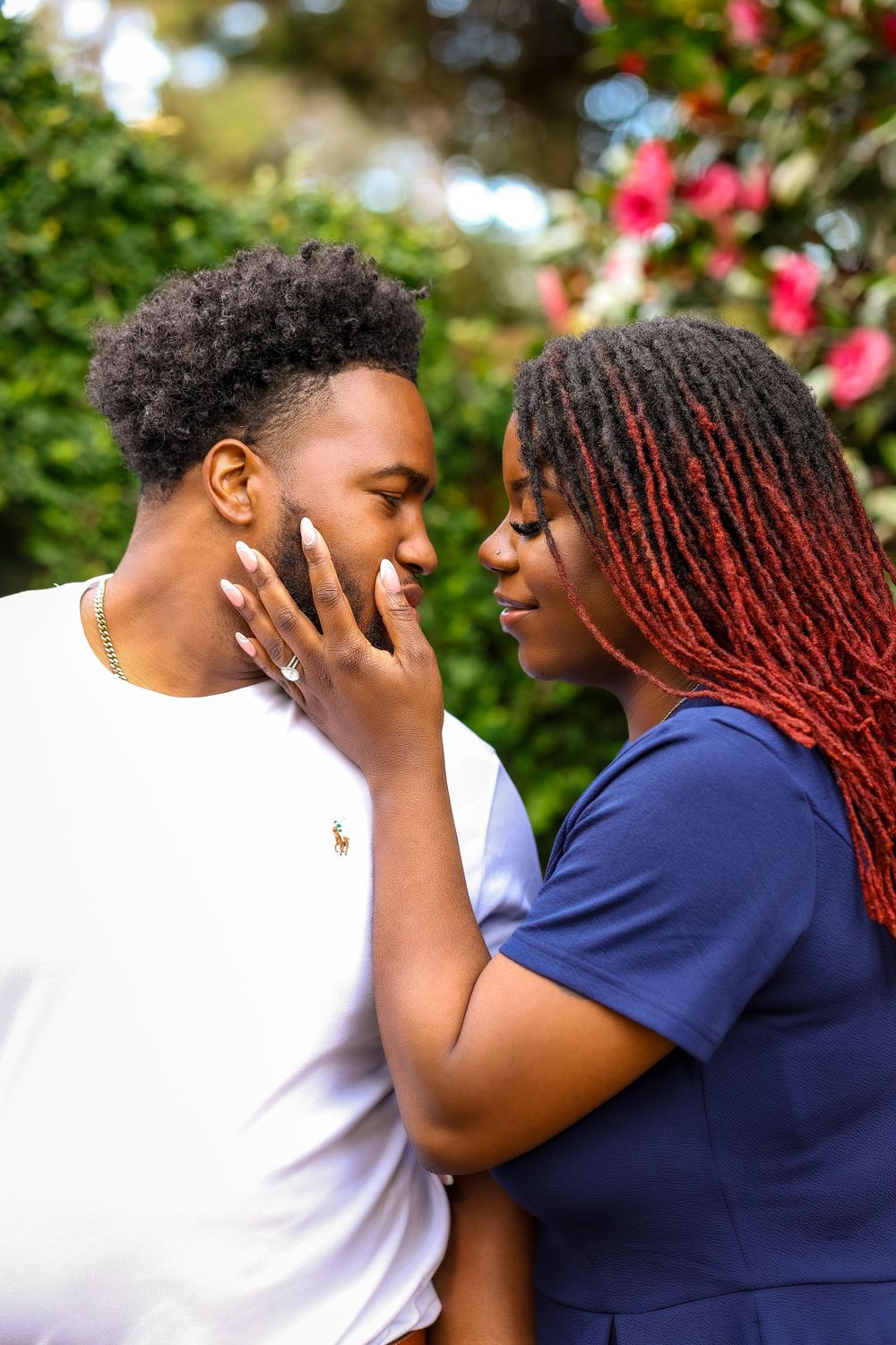 A tender romantic moment shared between a couple in a garden with pink flowers in the background.