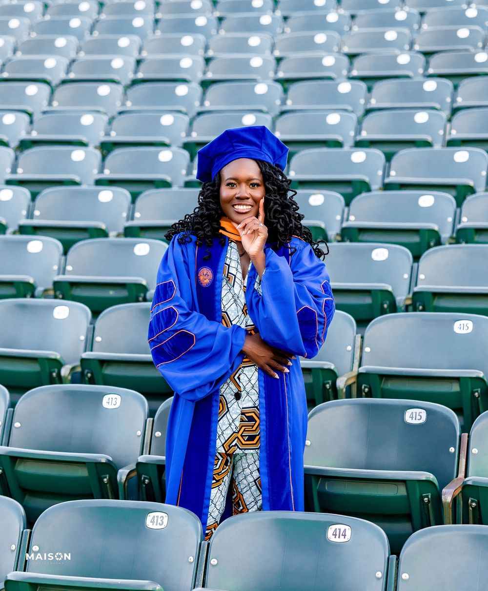 Graduate in bright royal blue academic regalia poses joyfully between empty stadium seats on graduation day.
